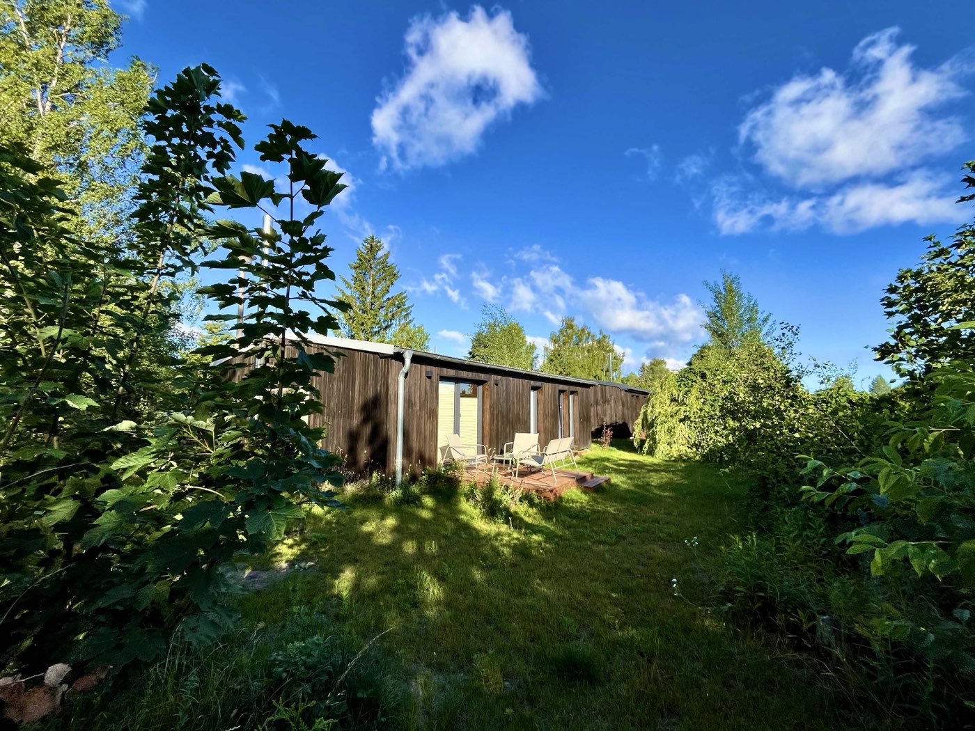 Haus 1 — schwarzes Holzhaus mit Garten unter blauem Himmel