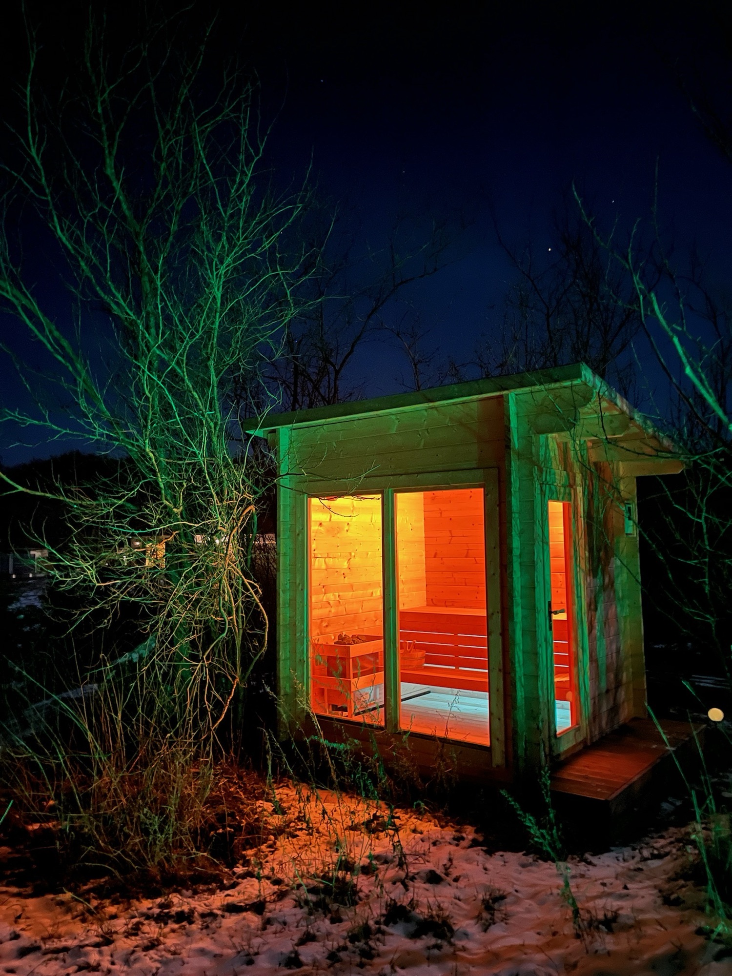 Gartensauna nachts, warm erleuchtet im Schnee